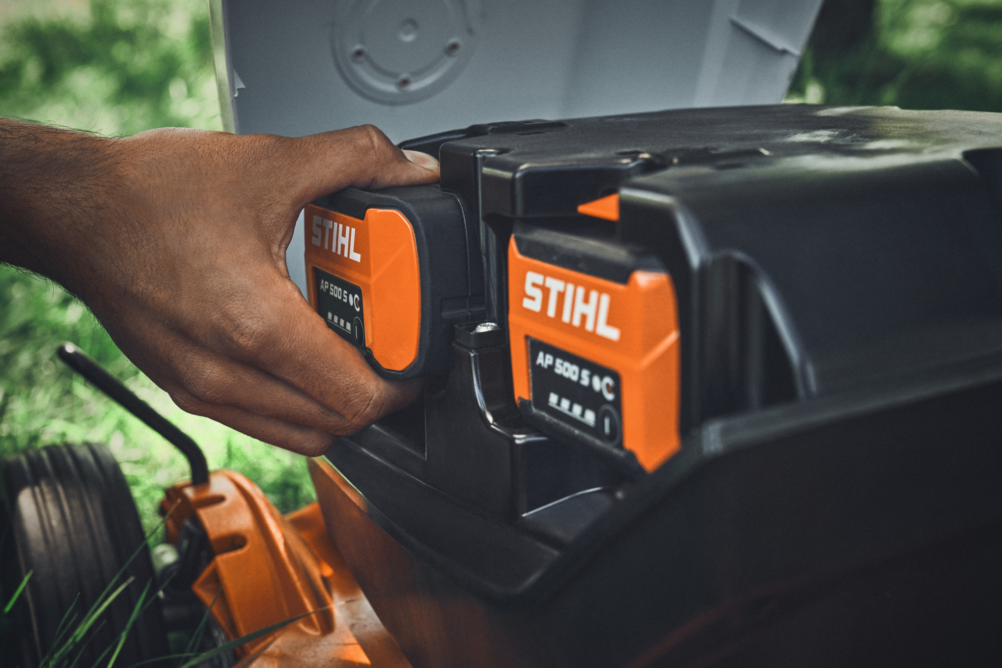 En person sätter i ett STIHL AP 500 S batteri i en STIHL sladdlös gräsklippare