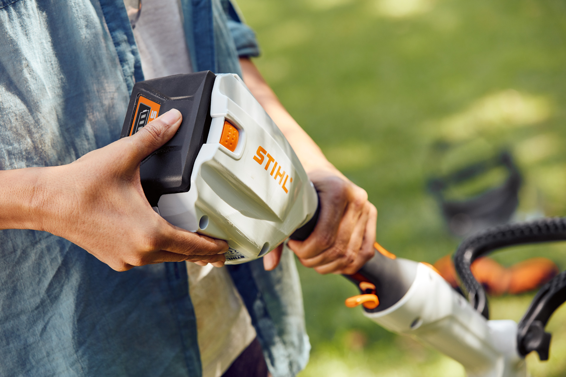 En person håller i STIHL FSA 56 batteridriven trimmer och för handen över batteriet