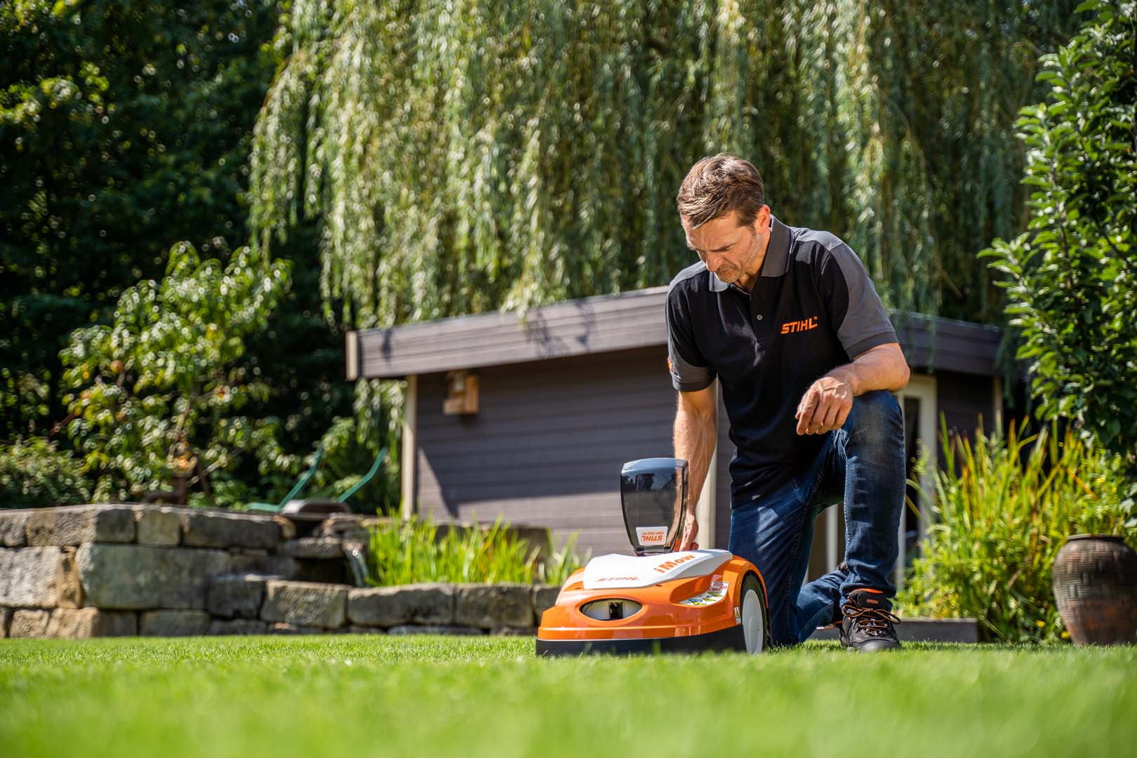 En STIHL-återförsäljare sitter på huk för att justera inställningar på en STIHL RMI 422 iMOW® robotgräsklippare i en trädgård