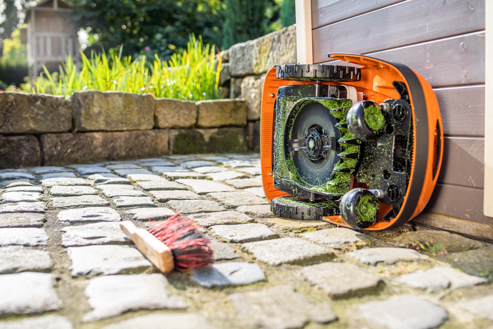 En STIHL iMOW® robotgräsklippare vänd på sidan redo för rengöring, med en intilliggande borste på marken