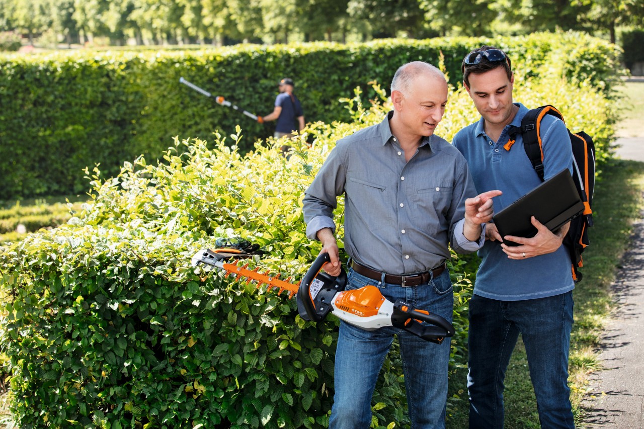 Man med STIHL hörselskydd i trädgården framför staplade stockar