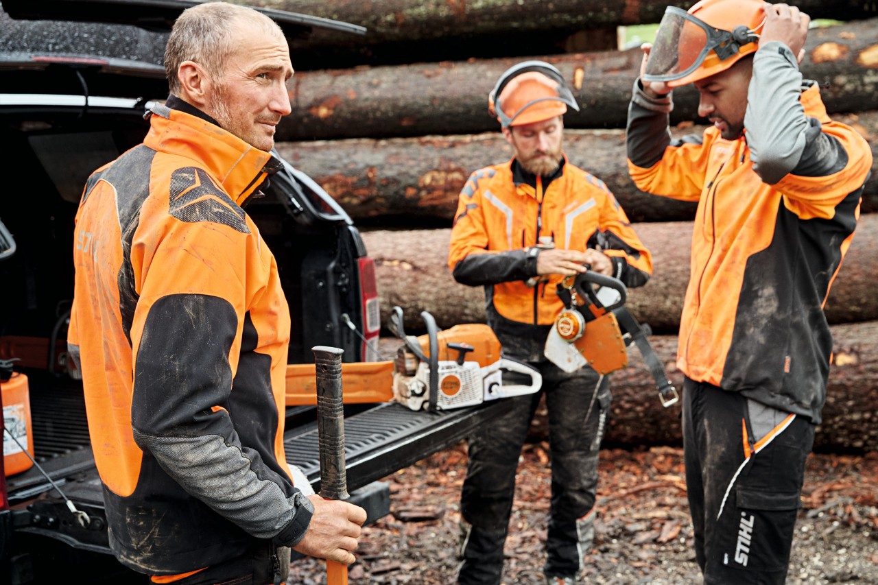 Tre män med skyddsutrustning framför ett fordon med öppet bagageutrymme med STIHL batteridrivna maskiner