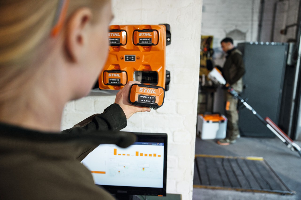 En kvinna framför en bärbar dator som tar bort en AP 300 S från en STIHL AL 301-4 multiladdare