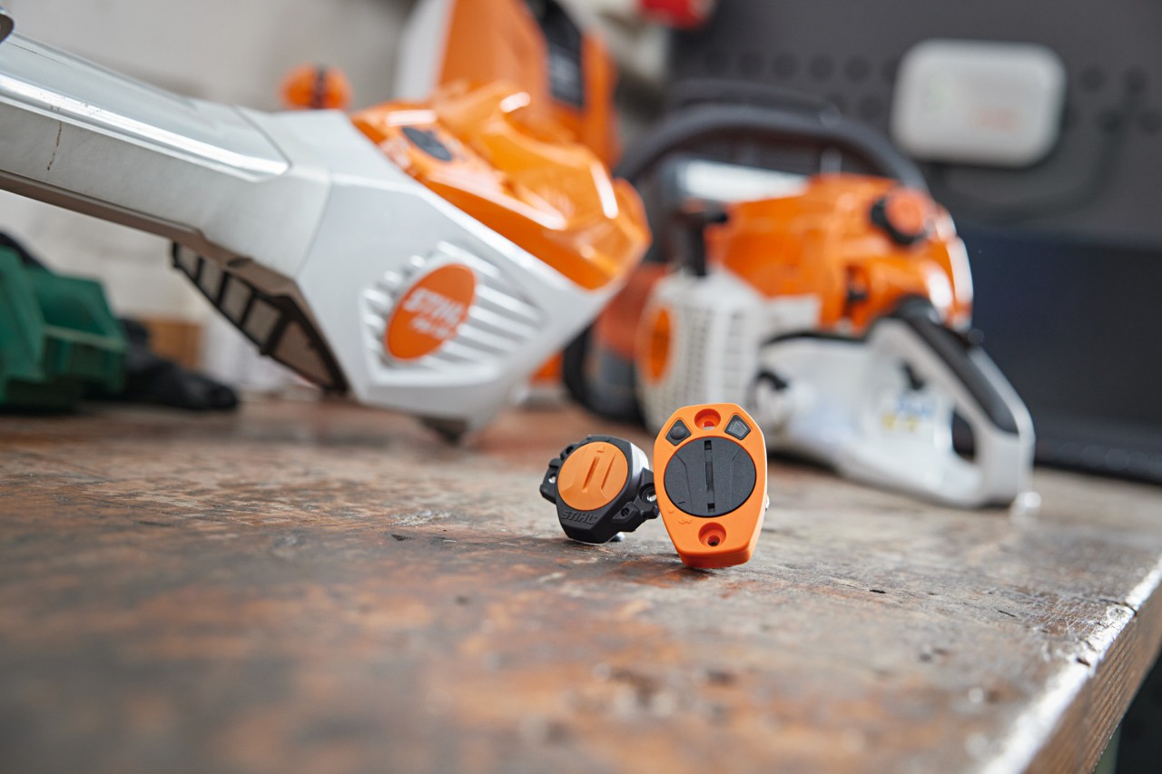 STIHL Smart Connector och STIHL Smart Connector 2 A på en arbetsbänk. Olika redskap från STIHL kan ses i bakgrunden.