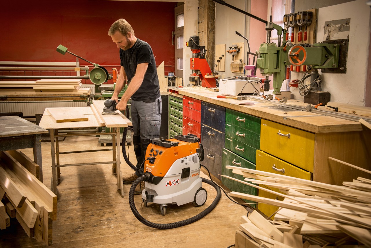 Man som använder en STIHL SE 133 ME våt- och torrdammsugare i en verkstad medan han arbetar med träplankor