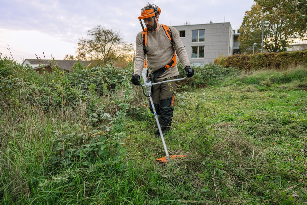 En man med STIHL skyddsutrustning klipper en vildvuxen grönyta med en batteridriven röjsåg STIHL FSA 200