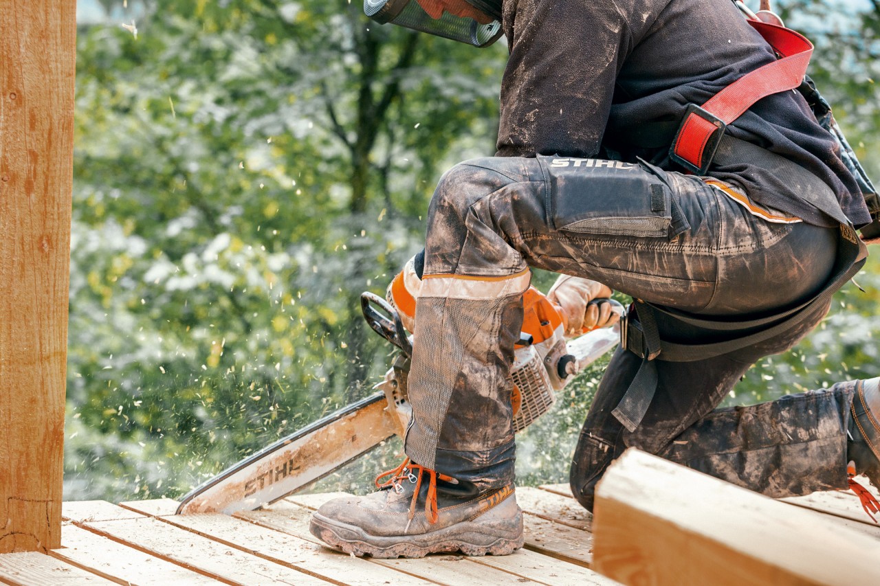 En person med arbetsstövlar och STIHL Advance X-Light byxor sågar till kanten på en träplattform med en STIHL motorsåg