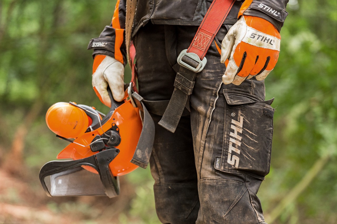 En person som bär STIHL arbetsbyxor och handskar och håller i en hjälm 