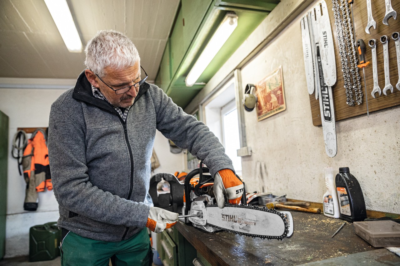 En man i en verkstad som skruvar fast ett sågsvärd av typen STIHL Rollomatic E på en motorsåg 