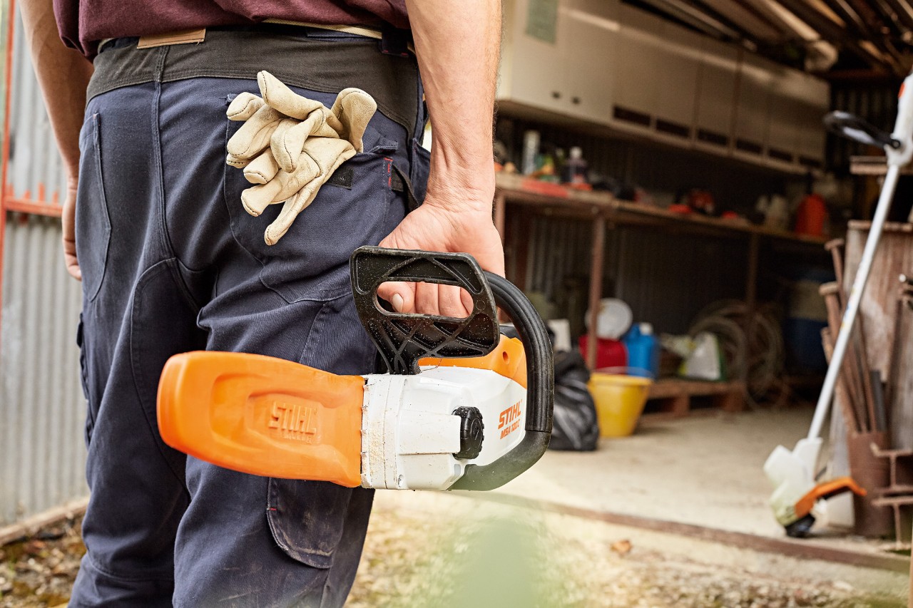 En man håller i en STIHL batteridriven motorsåg med svärd, i bakgrunden står en STIHL batteridriven trimmer i verkstaden