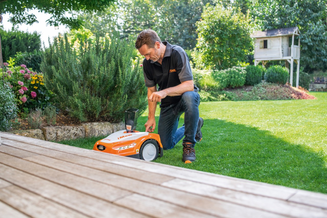 En STIHL-återförsäljare använder kontrollpanelen på en STIHL iMOW® 422 robotgräsklippare i en trädgård