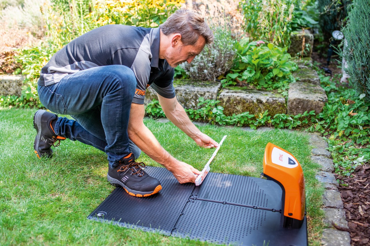 En STIHL-återförsäljare monterar dockningsstationen för en STIHL iMOW® 422 robotgräsklippare i en trädgård