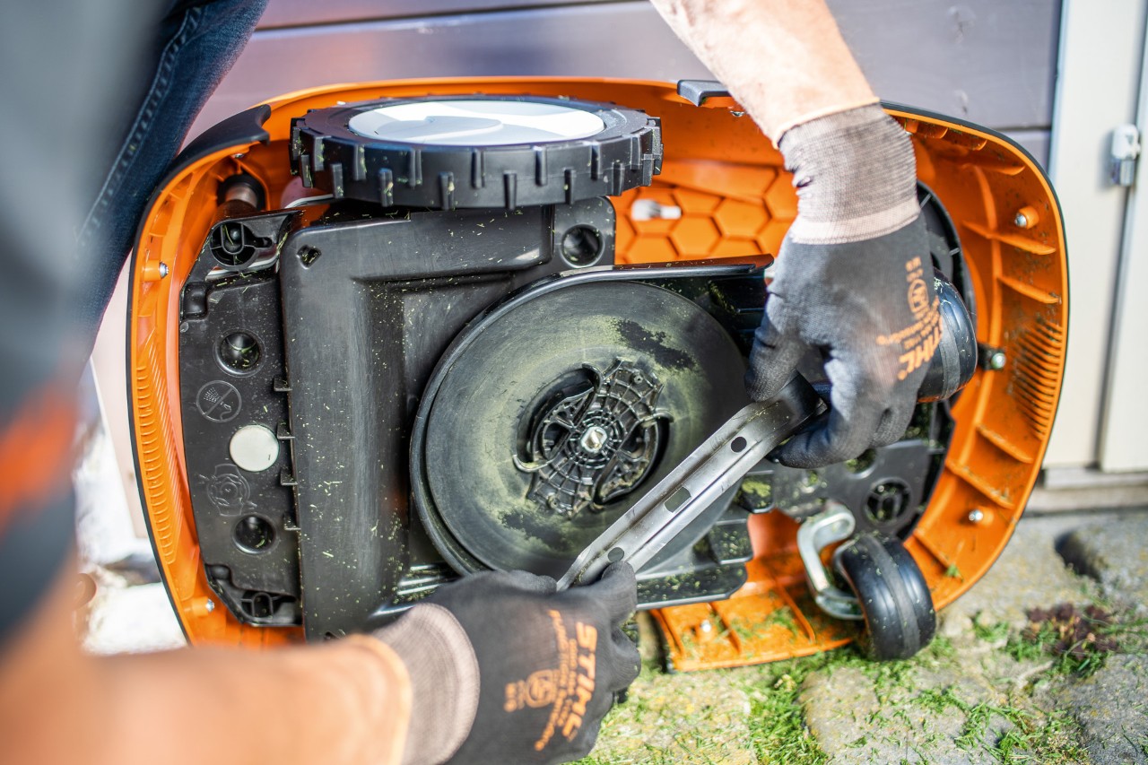 En person inspekterar knivbladet på en STIHL iMOW® robotgräsklippare som ligger på sidan