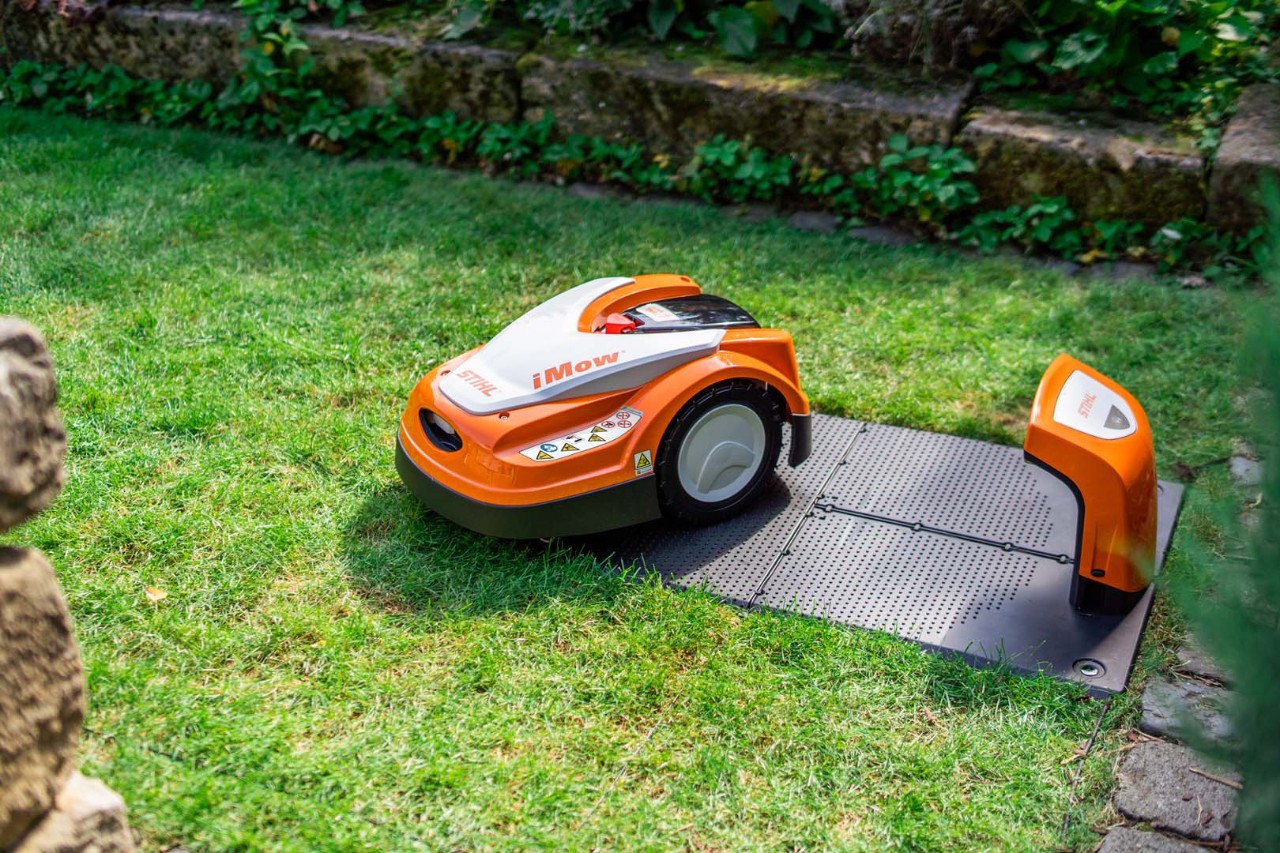 En STIHL iMOW® robotgräsklippare bredvid sin dockningsstation på en grön gräsmatta