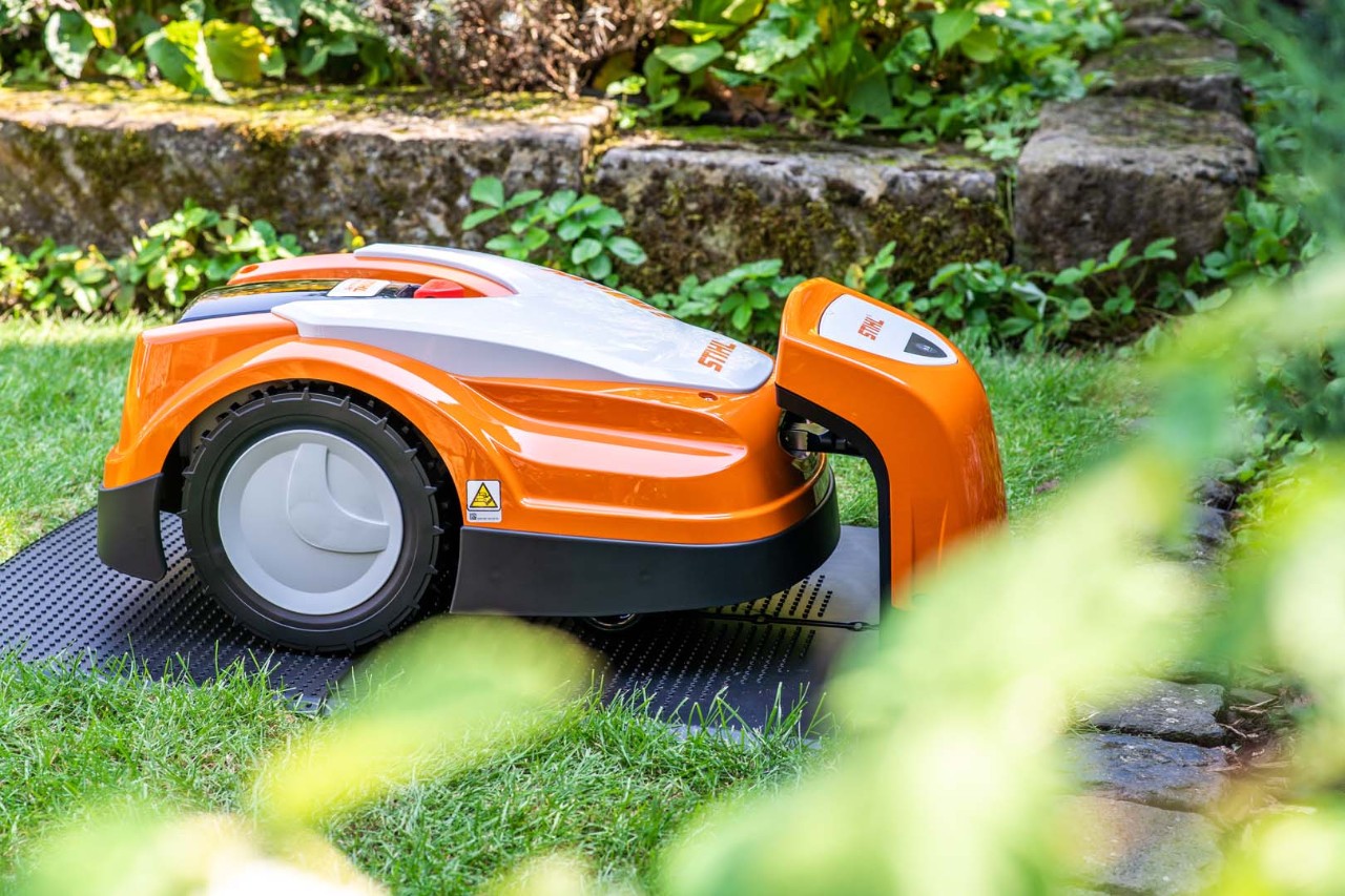 En STIHL iMOW® 422 robotgräsklippare i en trädgård laddas i sin dockningsstation