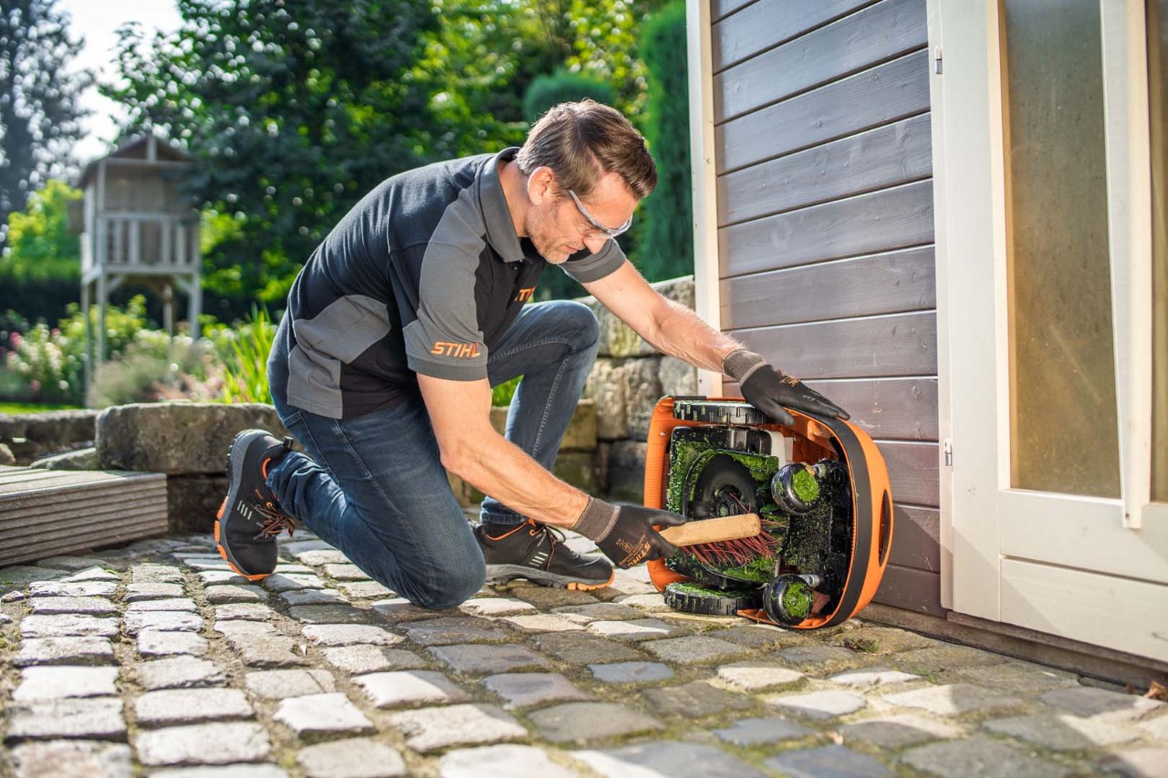 En man använder en borste för att rengöra undersidan av en STIHL iMOW® 422 robotgräsklippare 