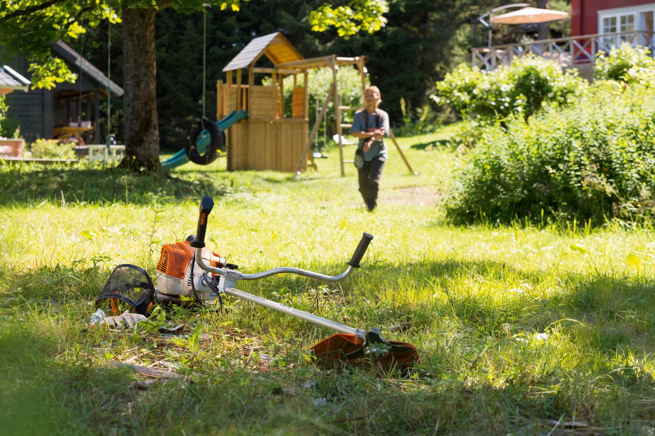 STIHL trimmer FS 240 ligger i gräset, i bakgrunden förbereder en man för underhåll