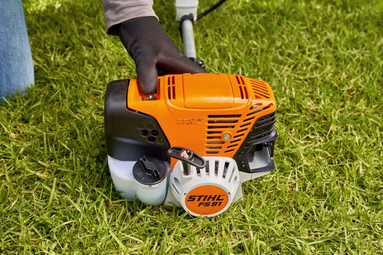 En man trycker på bränslepumpen på STIHL FS 91 bensindriven trimmer för att starta den