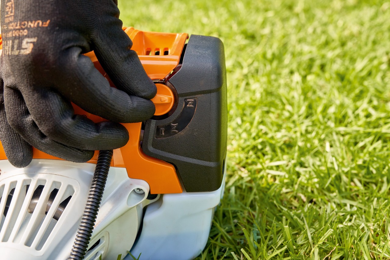 En man ställer in spaken på bränslepumpen på STIHL FS 91 bensindriven trimmer för att starta den