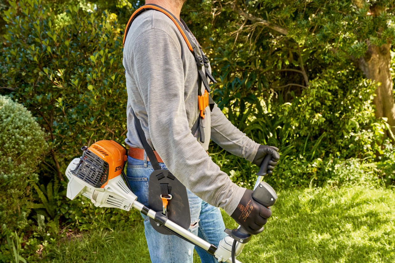 En man lyfter STIHL FS 91 bensindriven trimmer från marken för att börja klippa 