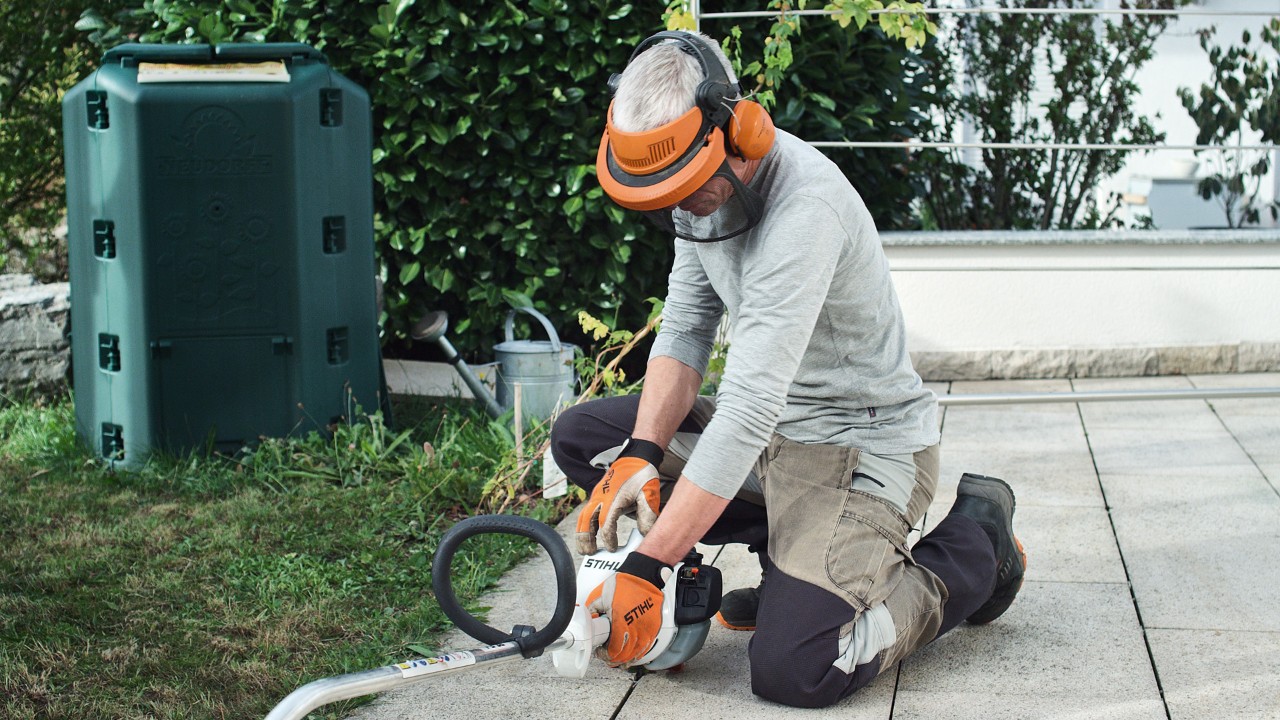 En person i skyddskläder trycker STIHL FS 38 bensindriven trimmer mot marken
