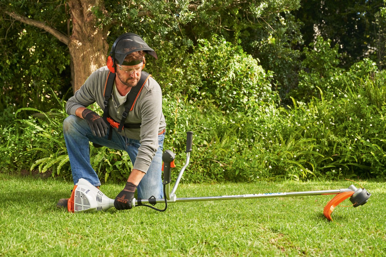 En man lägger STIHL FS 56 bensindriven trimmer på marken för att starta den