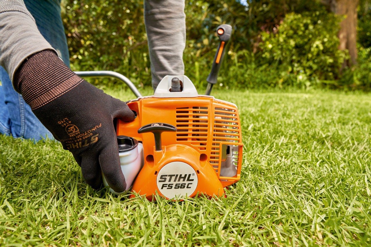 En man trycker på bränslepumpen på STIHL FS 56 bensindriven trimmer för att starta den