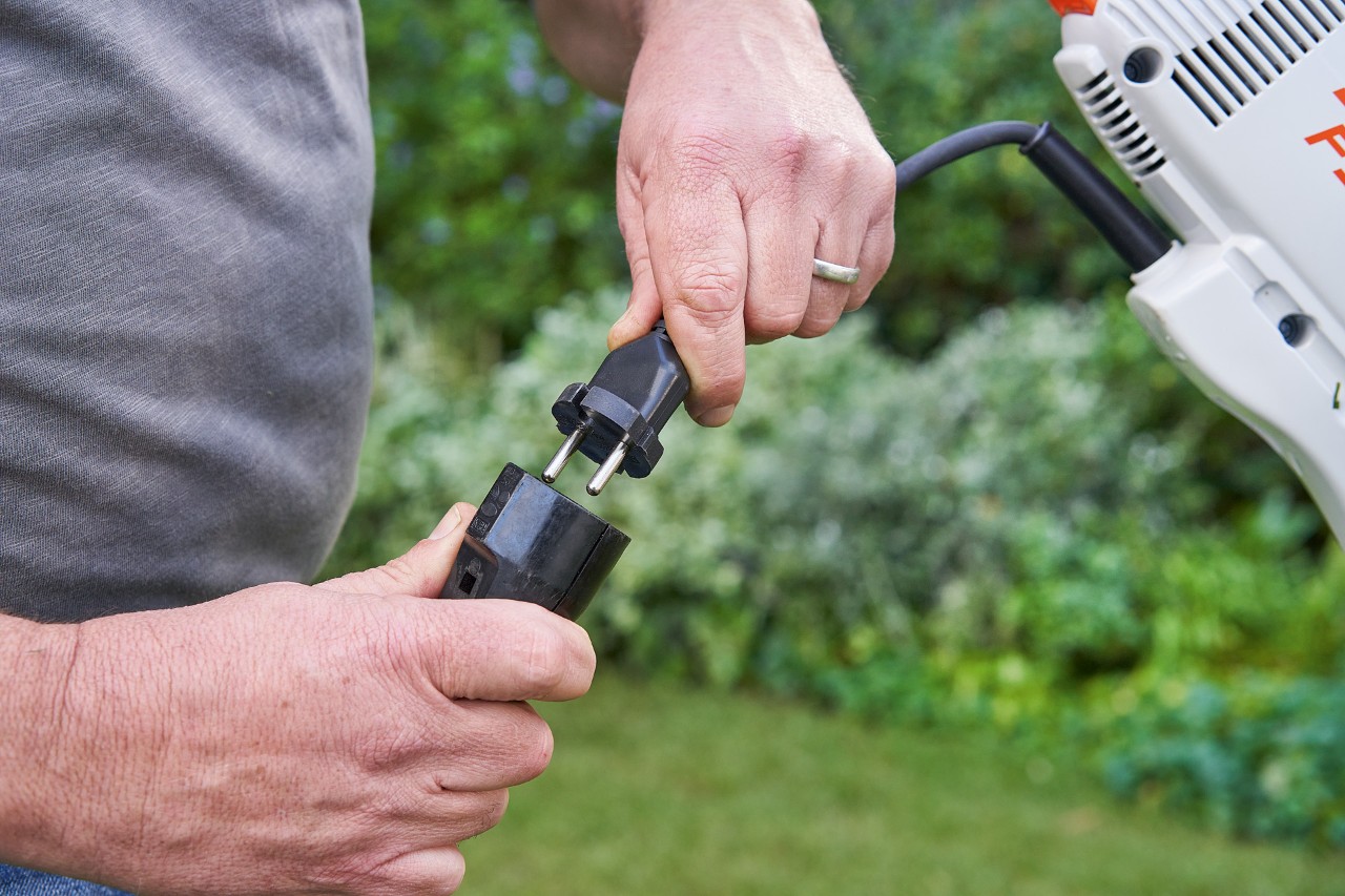 En man som bär skyddshandskar trycker på gasspaken på STIHL FSE 60 eletrisk trimmer för att starta den