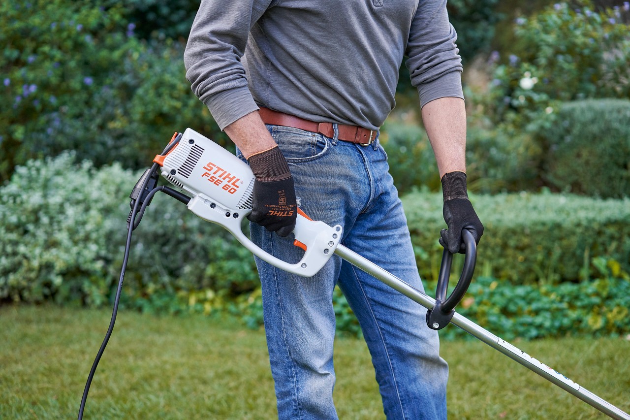 Man som bär skyddshandskar håller i STIHL FSE 60 elektrisk trimmer med båda händerna