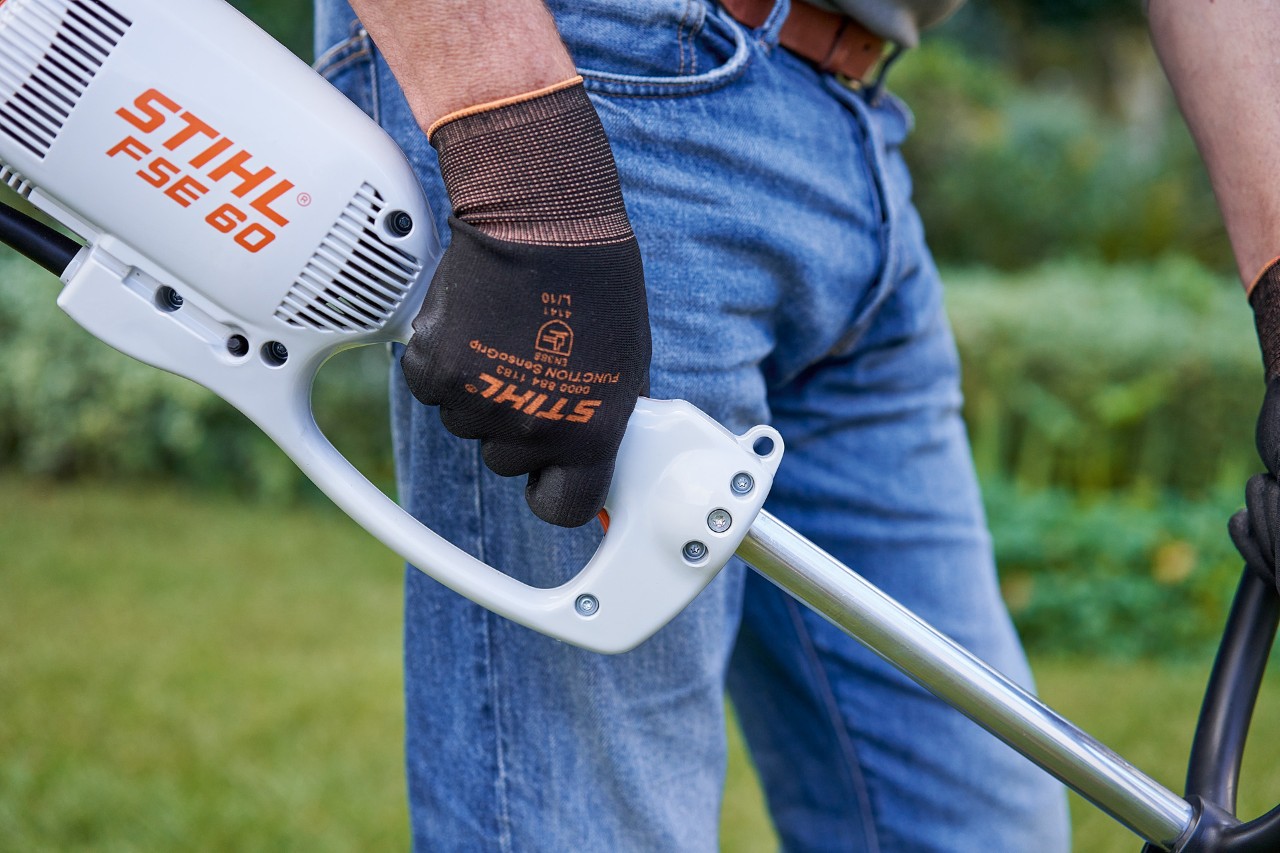 En man trycker på strömbrytaren på manöverhandtaget på STIHL FSE 60 elektrisk trimmer