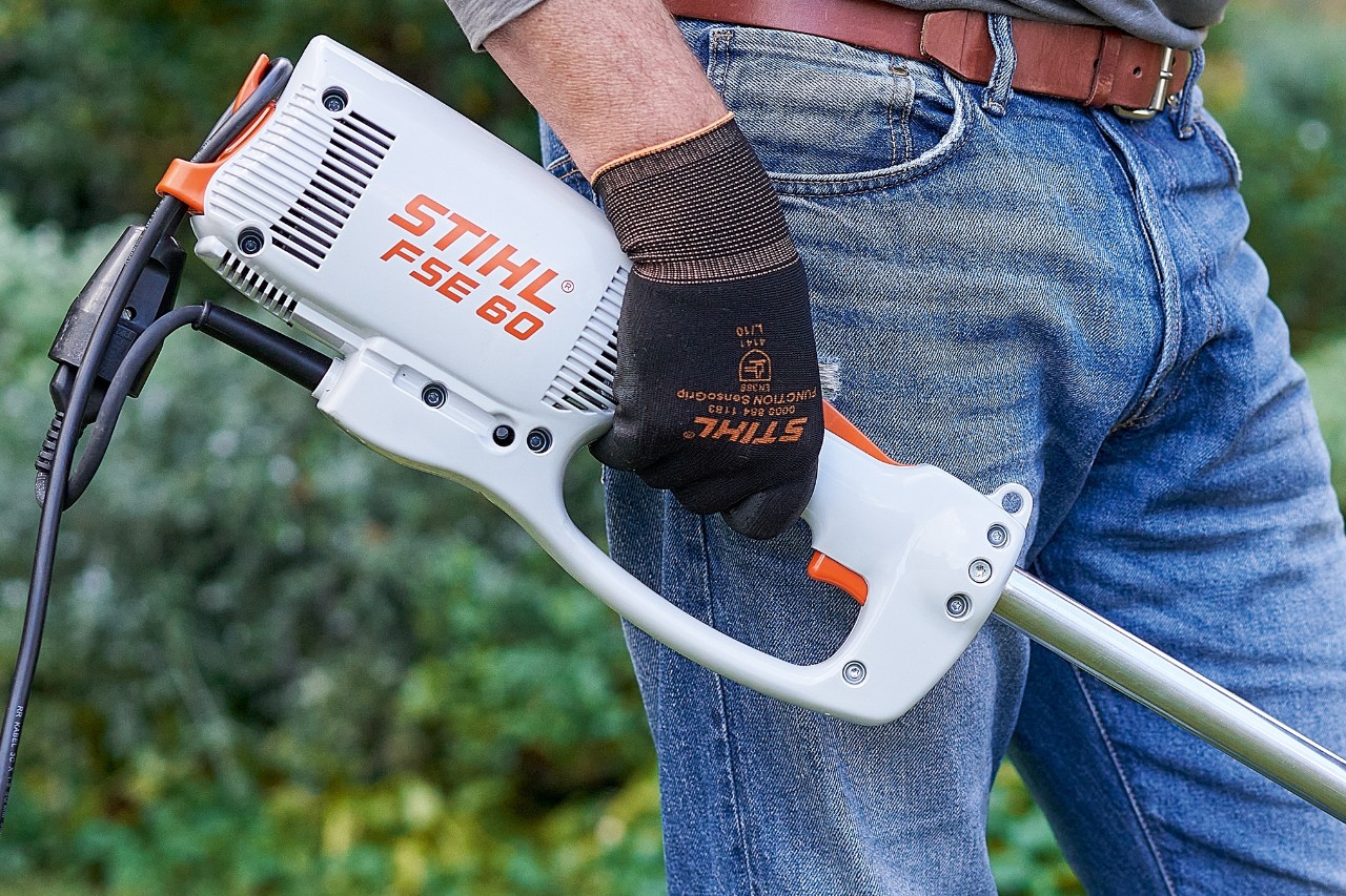 En man trycker på en brytare för att stänga av den elektriska trimmern STIHL FSE 60.