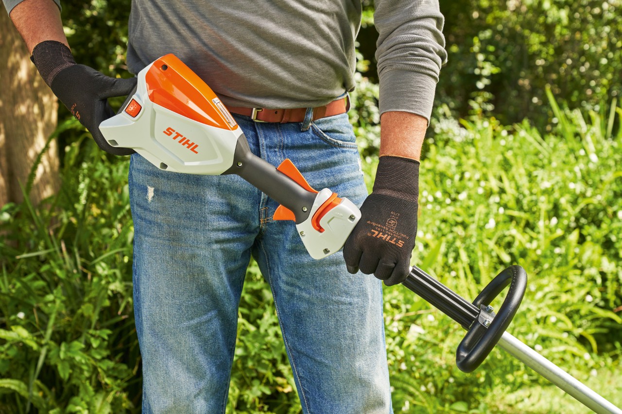 En man som bär skyddshandskar kontrollerar batteriet i STIHL FSA 60 batteridriven trimmer för att starta den