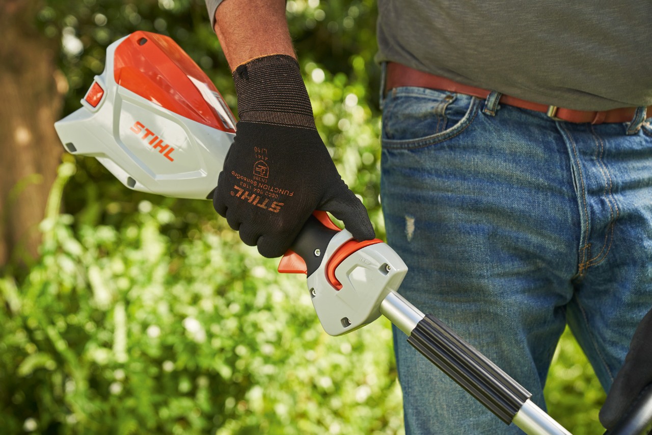 En man som bär skyddshandskar skjuter spärren på STIHL FSA 60 batteridriven trimmer till manöverhandtaget