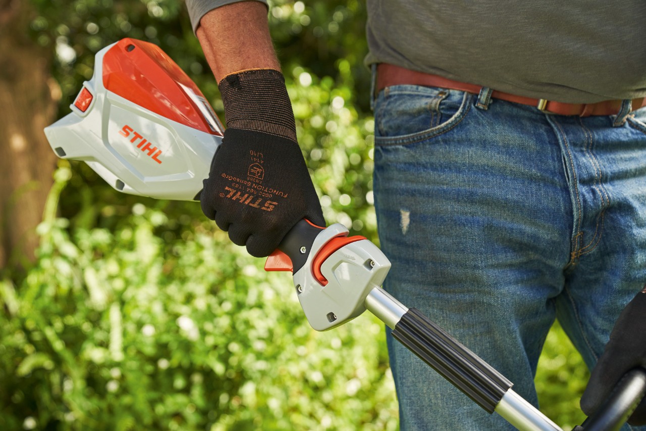 En man som bär skyddshandskar trycker på gasspaksspärren på STIHL FSA 60 batteridriven trimmer 