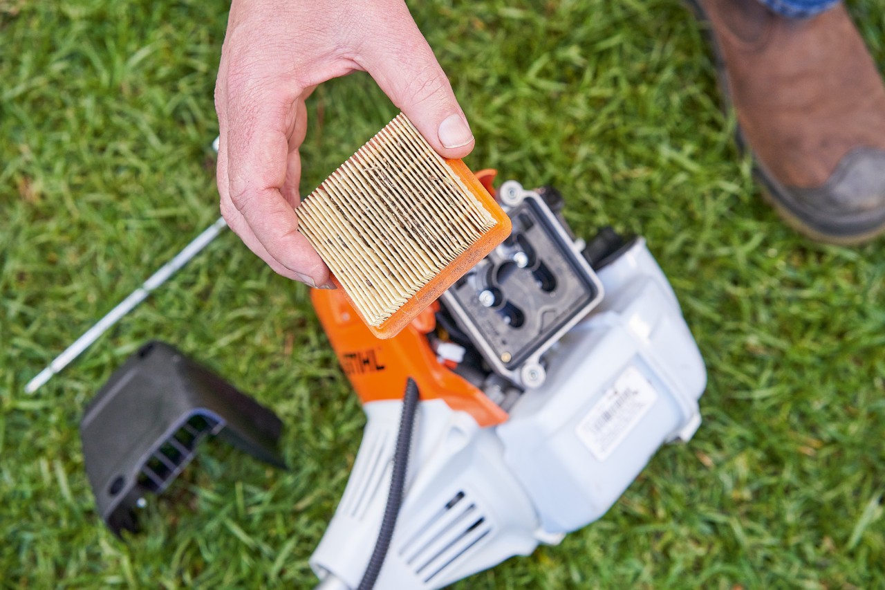 En person tar bort luftfiltret från en STIHL röjsåg för att rengöra det 