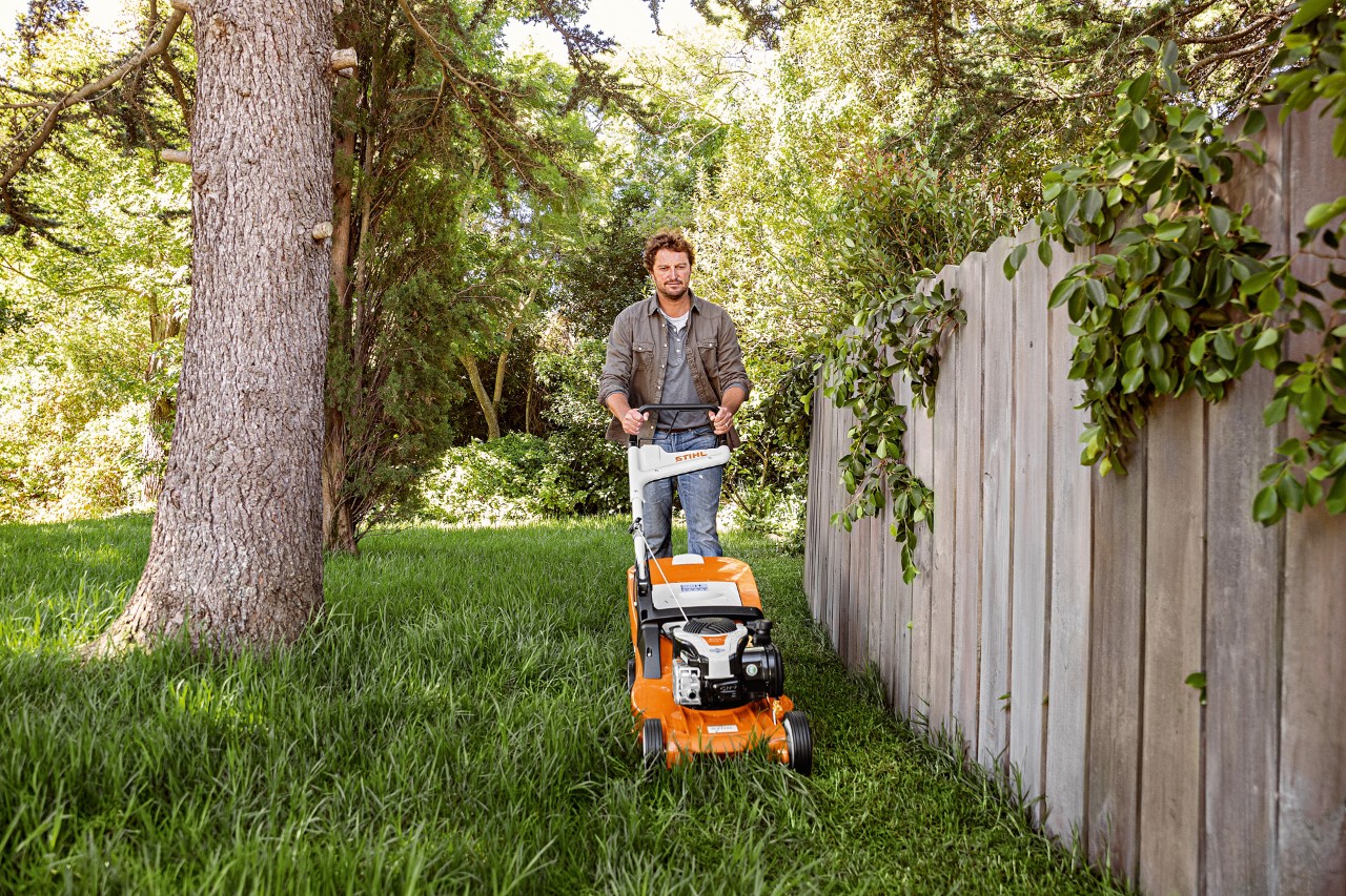 En man klipper gräset med bensingräsklipparen RM 448 TC från STIHL bredvid ett plank