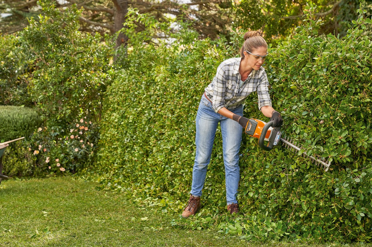 En kvinna använder STIHL HS 82 häcksax för att klippa en häck