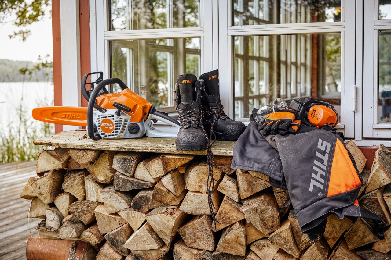 Stihl maskiner vilandes på en vedhög längsmed husvägg. 