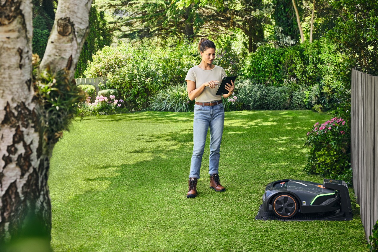 En kvinna som styr sin STIHL iMOW® EVO i trädgården via en surfplatta
