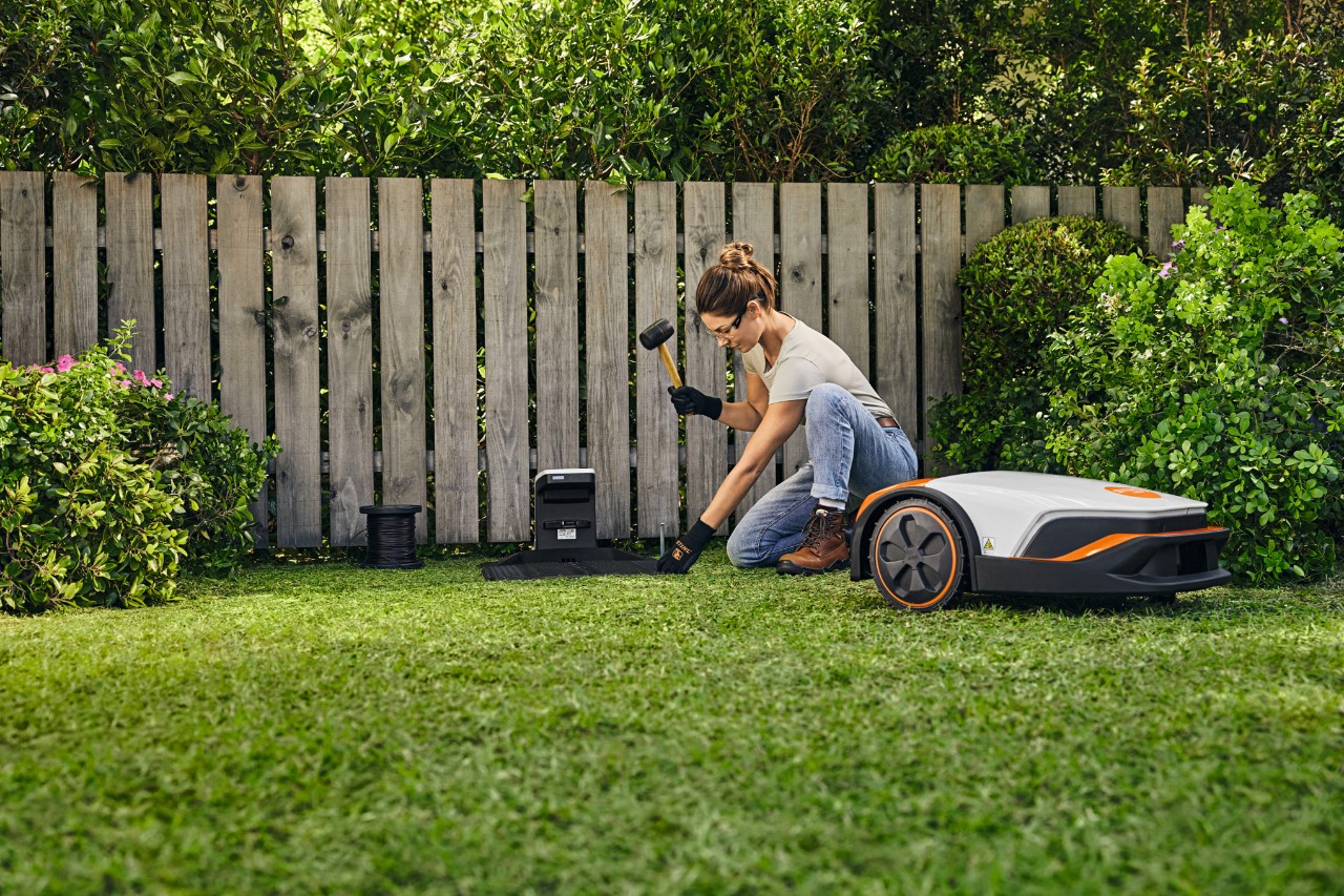 En kvinna installerar dockningsstationen för sin STIHL iMOW® framför ett staket i sin trädgård.