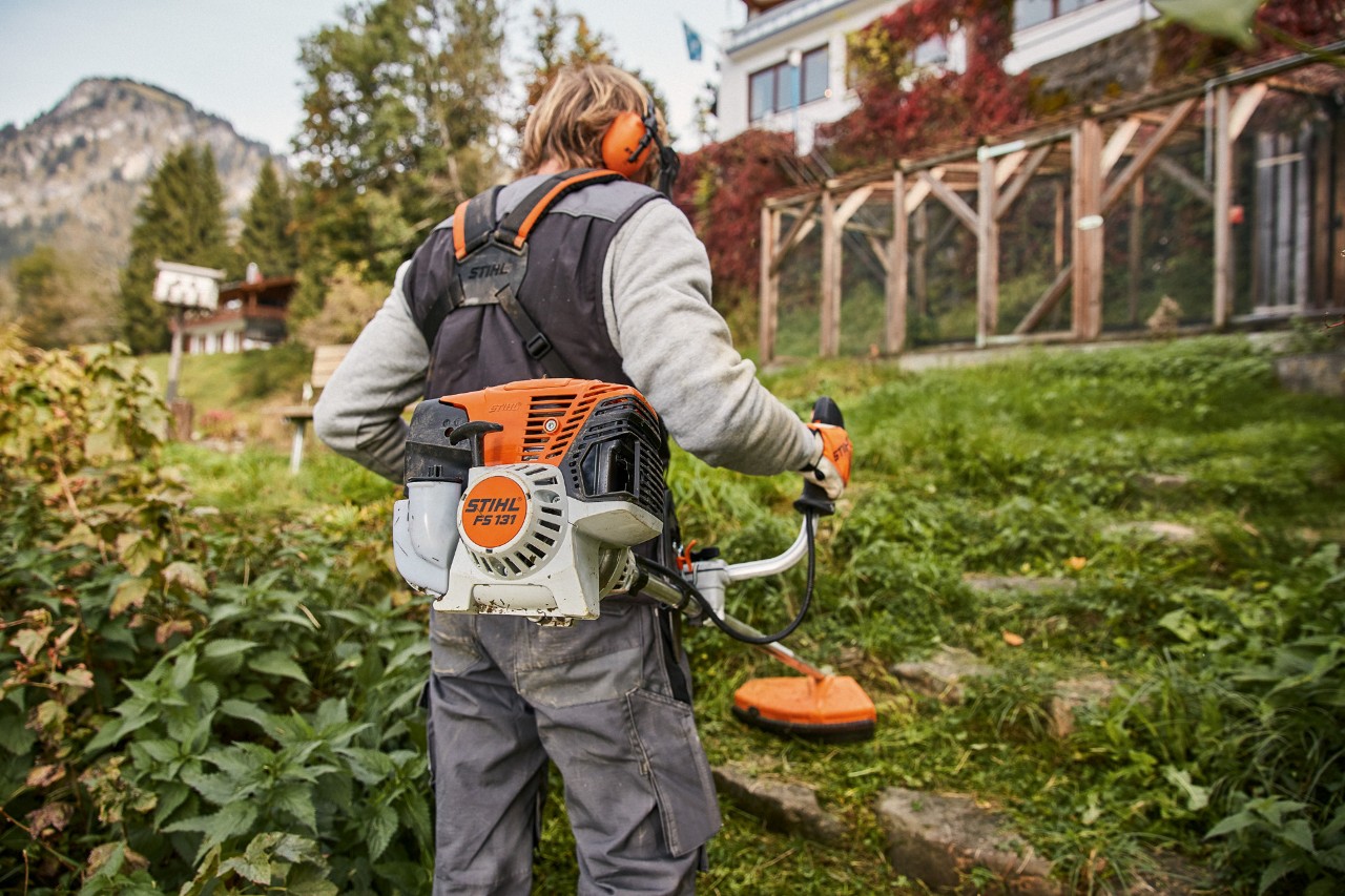 Sluttande mark framför ett hus bearbetas med den bensindrivna trimmern med 4-taktmotor, STIHL FS 131 med en STIHL 4-Mix®-motor 